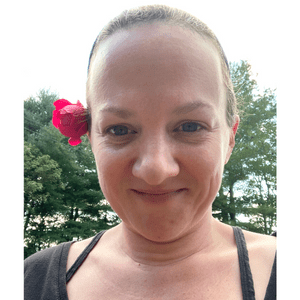 A photo of Amber Shehan smiling at the camera with a red flower behind her right ear.