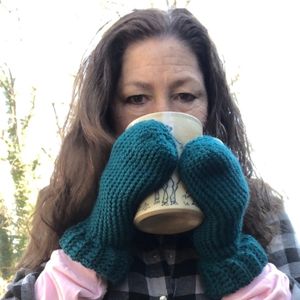A photo of Janet Garmen drinking from a coffee cup with mitten covered hands. 